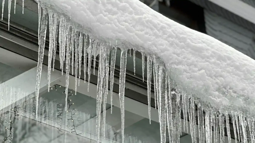 Ice dam and icicle buildup along roof edge and gutters causing winter roof damage in Rochester MN