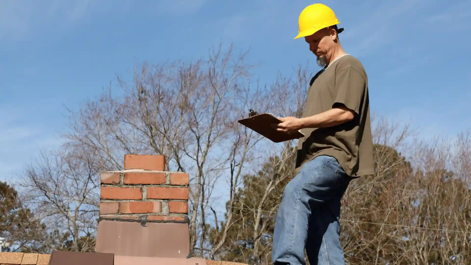 Roofing contractor with clipboard inspecting residential roof and chimney in Rochester MN